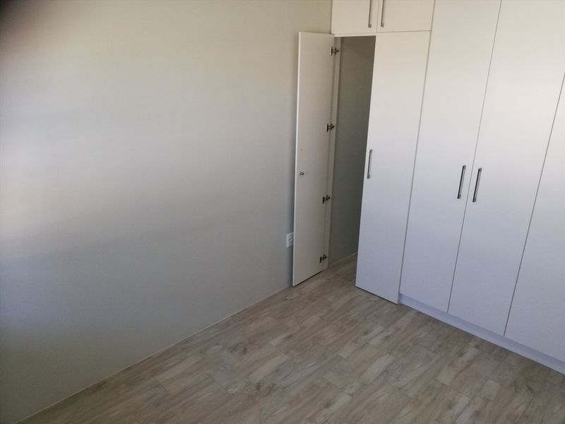 A clean, empty bedroom featuring modern light-toned laminate flooring and ample built-in cupboard storage with white cabinetry.