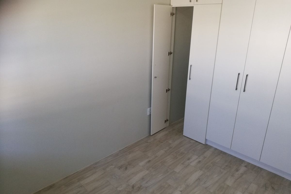 A clean, empty bedroom featuring modern light-toned laminate flooring and ample built-in cupboard storage with white cabinetry.