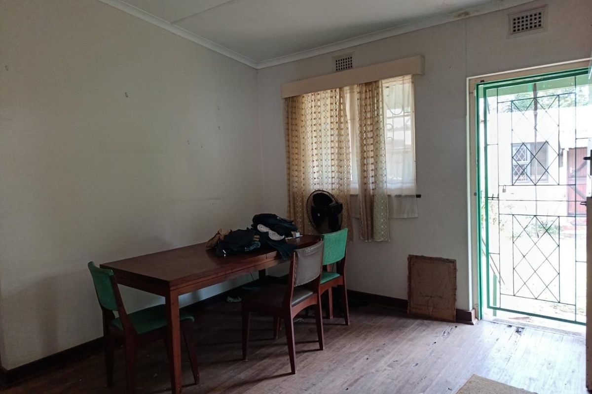 A living area featuring timber flooring, a security gate entrance, and ceiling air vents, requiring cosmetic updates to improve its overall condition.