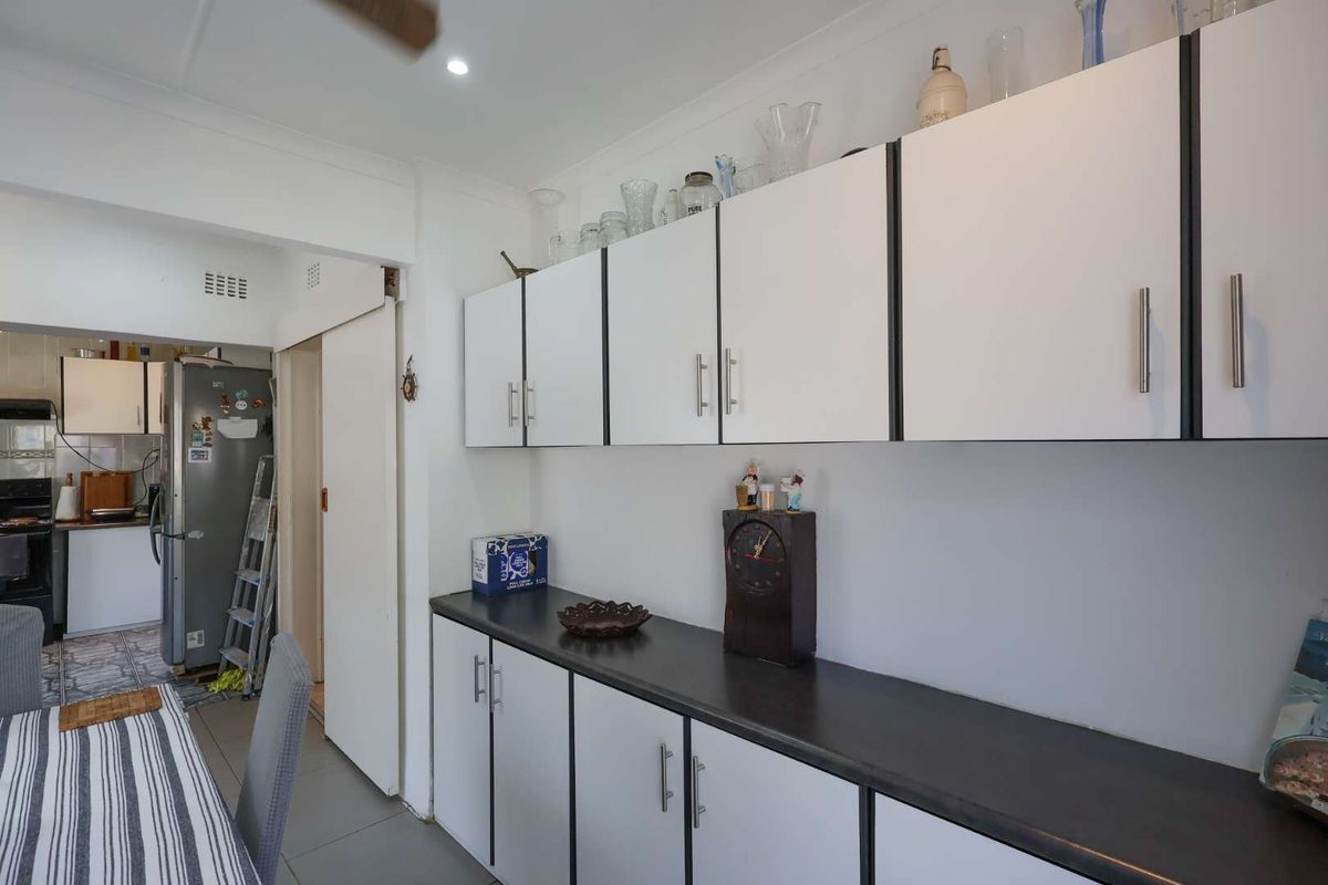 A functional kitchen area featuring white cabinetry with dark trim, dark laminate countertops, and tiled flooring, with an adjacent scullery or prep space visible.