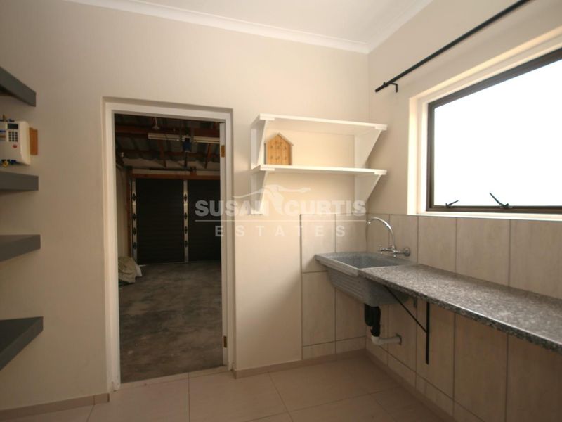 A functional laundry area featuring a utility sink, stone countertop, tiled backsplash, and wall-mounted shelving, with direct access to the garage.