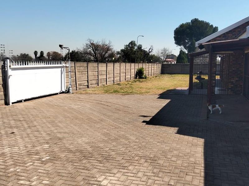 Spacious rear exterior area featuring a paved driveway, covered patio, and secure perimeter walling with a sliding gate.