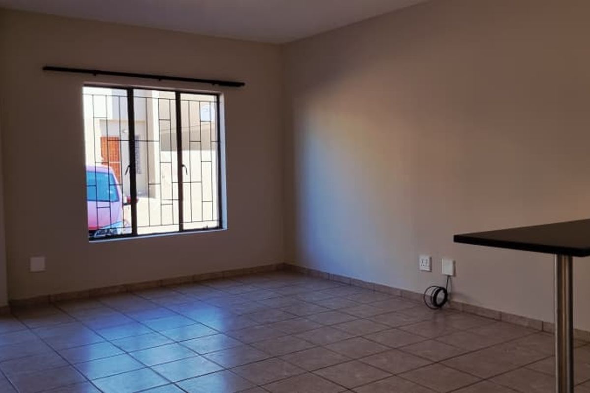 An open-plan living area featuring tiled flooring, a breakfast bar, and a window with security bars, offering a functional and versatile space.