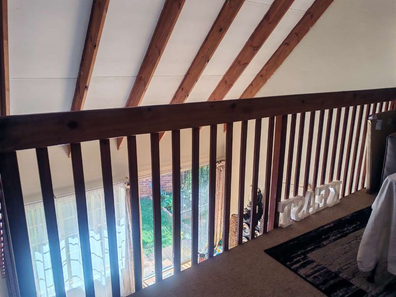 An elevated mezzanine hallway featuring exposed timber rafters and a wooden balustrade overlooking the lower level living area.