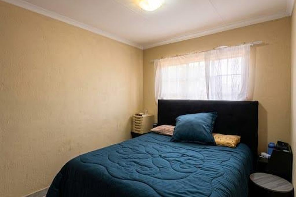 A compact bedroom featuring neutral wall finishes, a ceiling light fixture, and a window with fitted curtain rod.