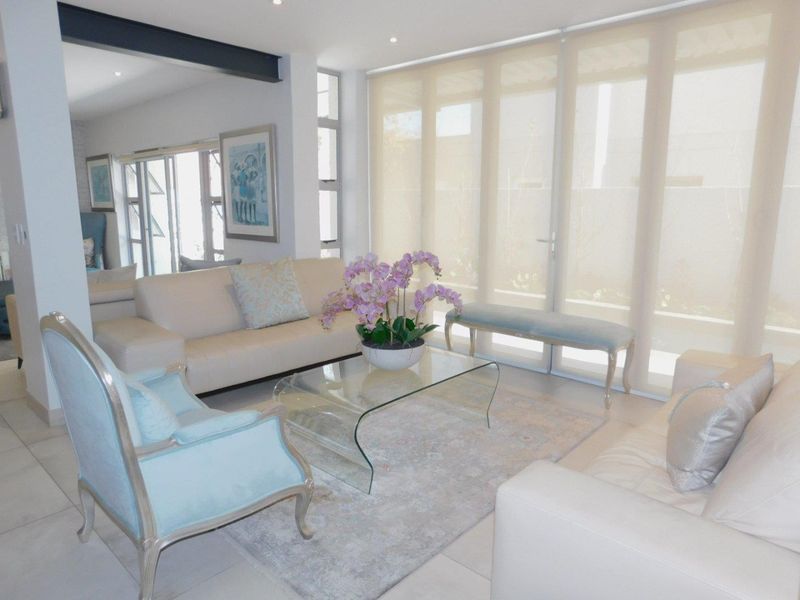 A bright and modern living room featuring large glass sliding doors with roller blinds, tiled flooring, and an exposed structural steel beam.