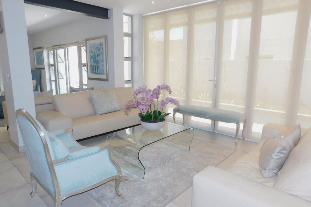 A bright and modern living room featuring large glass sliding doors with roller blinds, tiled flooring, and an exposed structural steel beam.