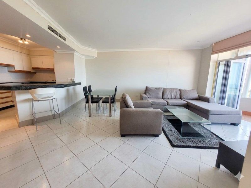 Spacious open-plan living and dining area featuring tiled floors, a breakfast bar, and direct access to a balcony through sliding glass doors.