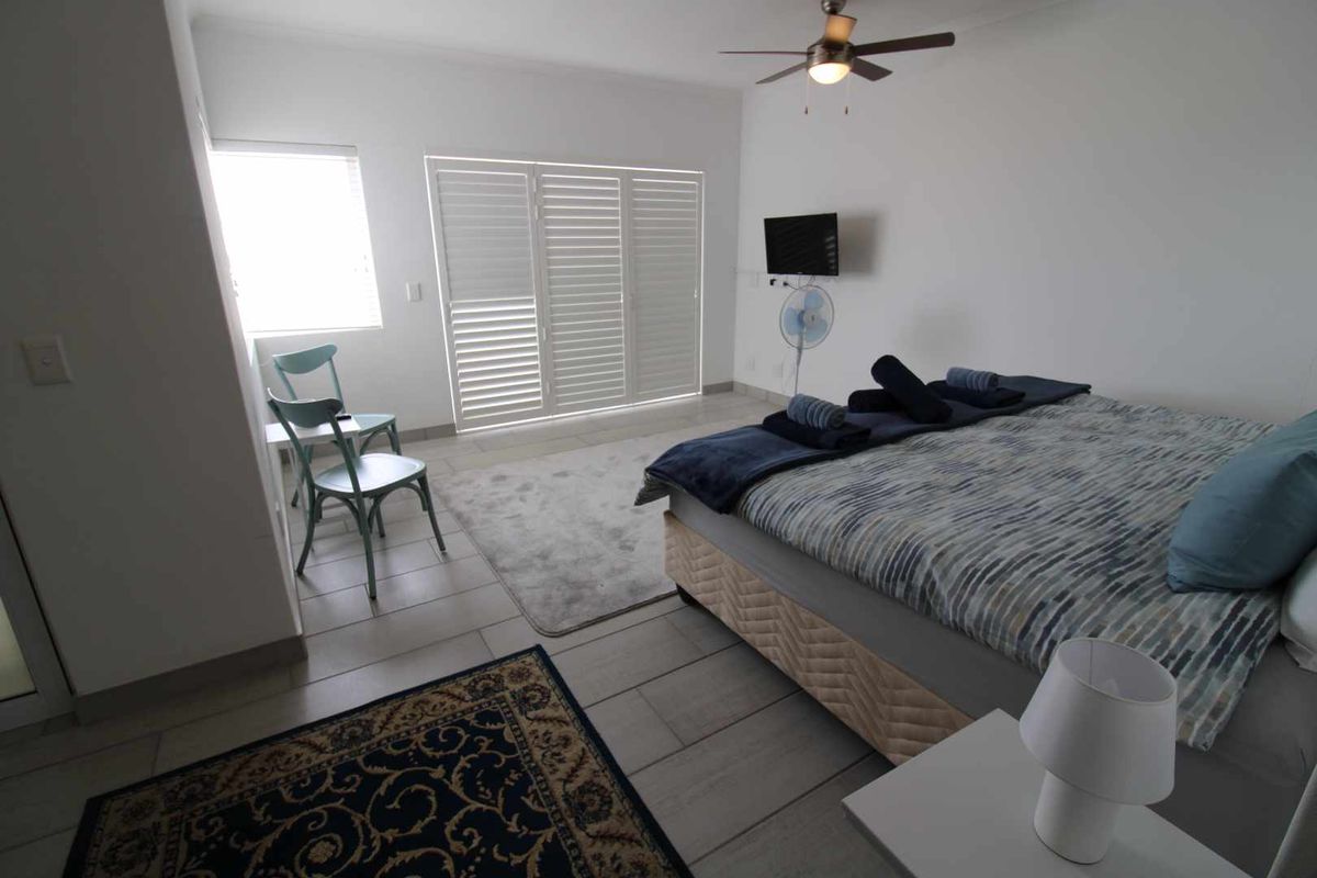 A well-maintained bedroom featuring tiled flooring, a ceiling fan, and white plantation shutters leading to an outdoor area.