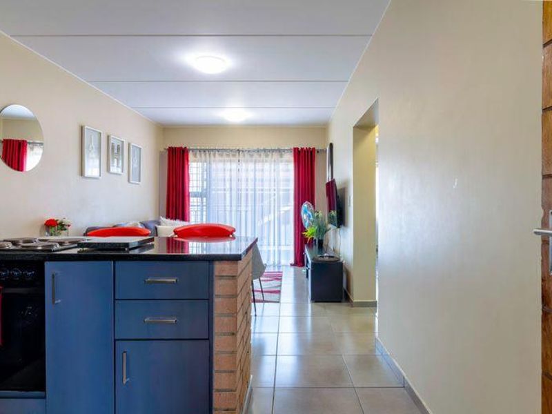 Open-plan living area featuring a kitchen with built-in oven and hob, tiled flooring, and a brick feature wall leading to a balcony.