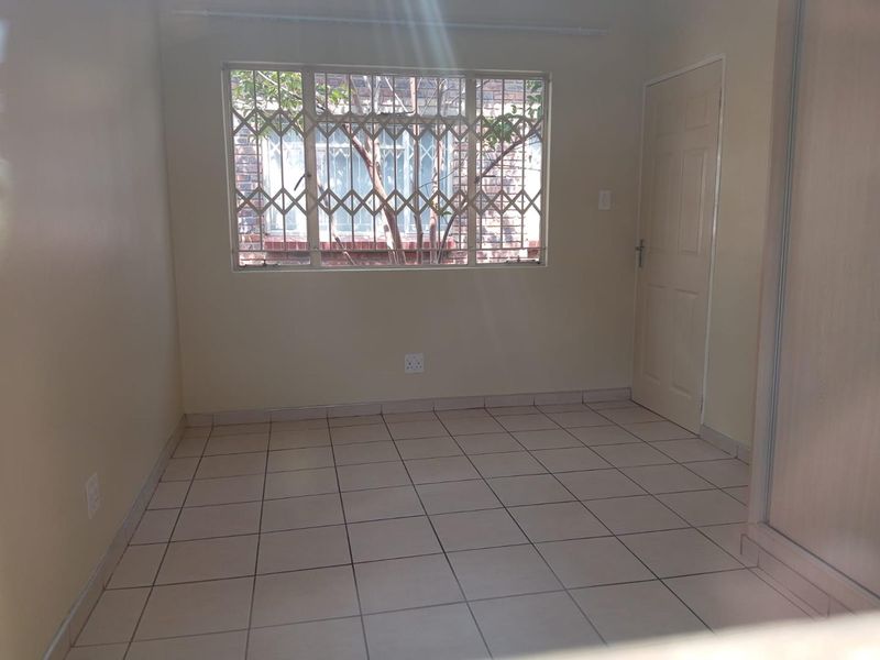 A clean, empty bedroom featuring tiled flooring, a built-in cupboard, and a window fitted with security burglar bars.