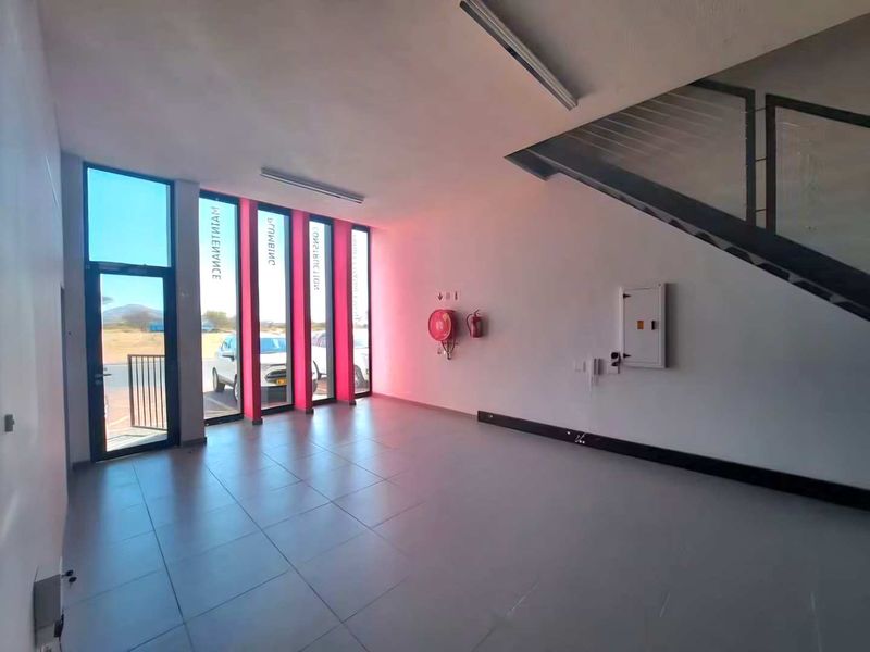 A spacious, empty entrance area featuring tiled flooring, large vertical windows, and a staircase, suitable for a professional office or commercial reception space.