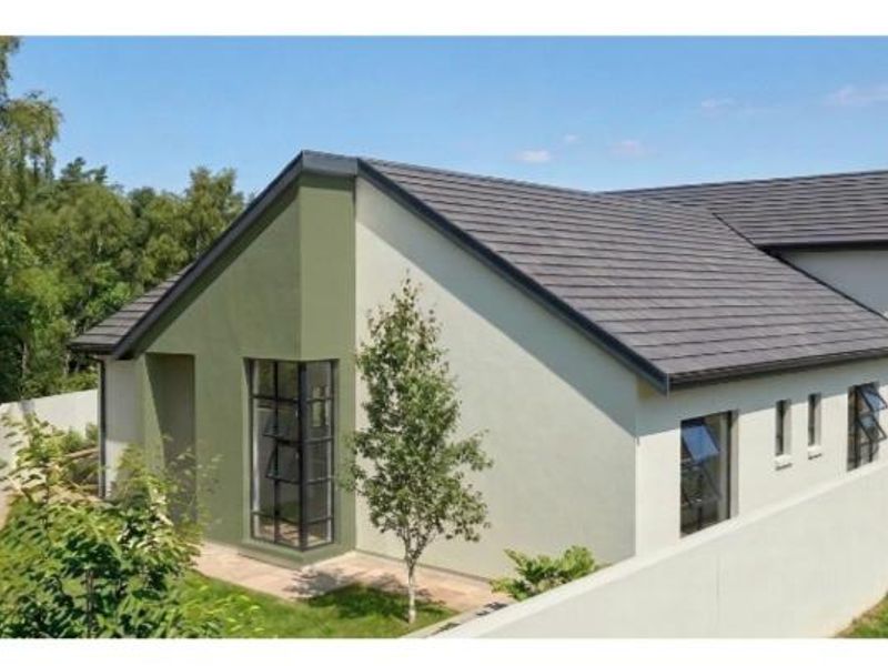 A well-maintained rear exterior view of the house featuring modern rendered walls, a tiled roof, and secure boundary walling.