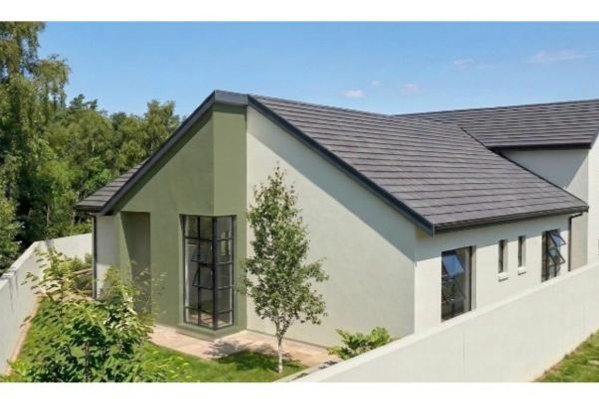 A well-maintained rear exterior view of the house featuring modern rendered walls, a tiled roof, and secure boundary walling.
