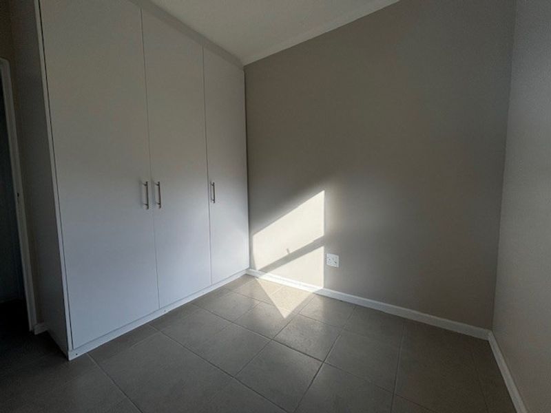 A clean, empty bedroom featuring neutral wall tones, modern tiled flooring, and ample built-in cupboard storage space.