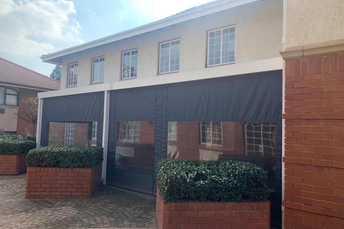 Exterior view of an office building featuring a covered patio area with roll-down weather blinds and integrated brick planter boxes.