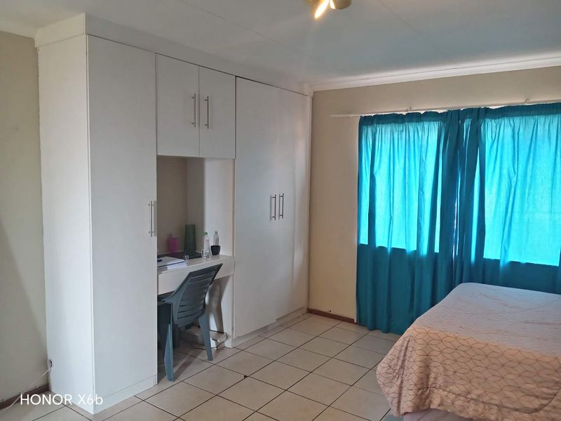 A bedroom featuring white built-in cupboards with an integrated desk space and tiled flooring.