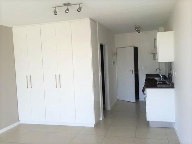 An open-plan living area featuring built-in cupboards, tiled flooring, and a compact kitchenette with a sink.
