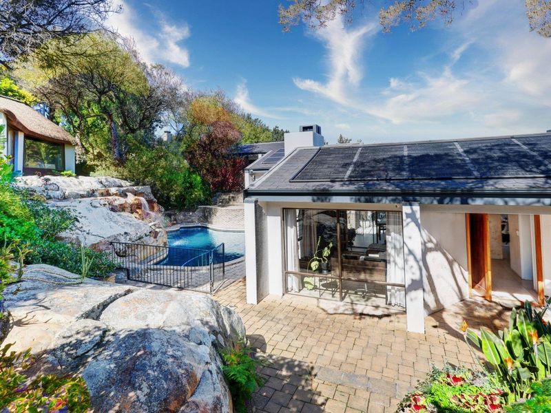 Rear exterior view featuring a paved patio, swimming pool, natural rock landscaping, and solar panels installed on the roof.