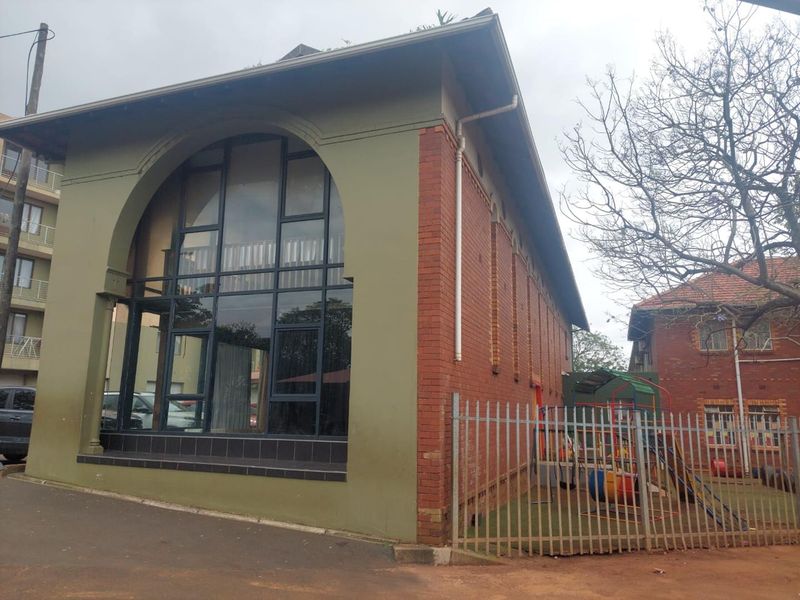 Exterior view of a building featuring a prominent arched window, brick facade, and metal security fencing.