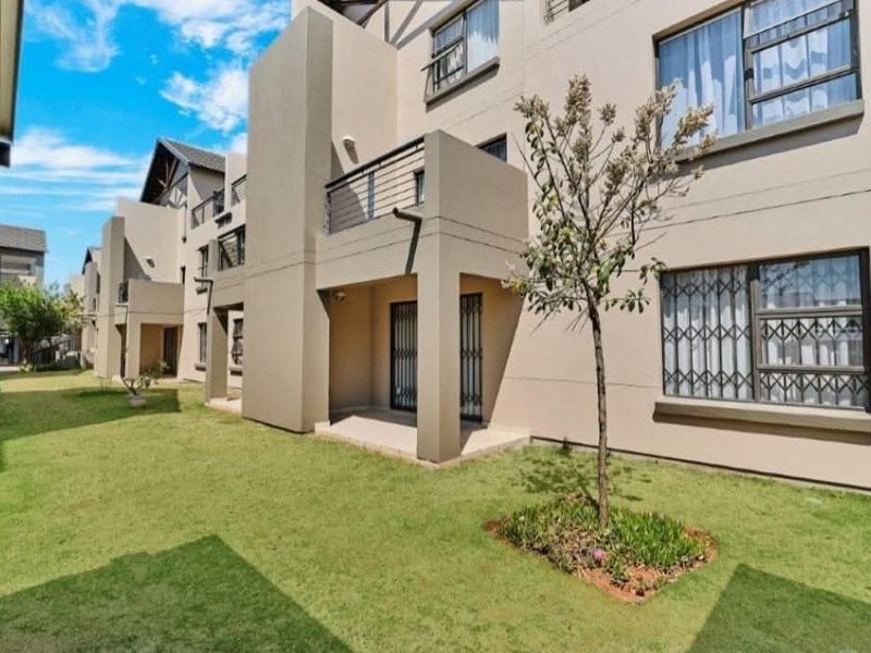 Rear view of a modern apartment complex featuring private balconies, security gates, and well-maintained communal garden areas.