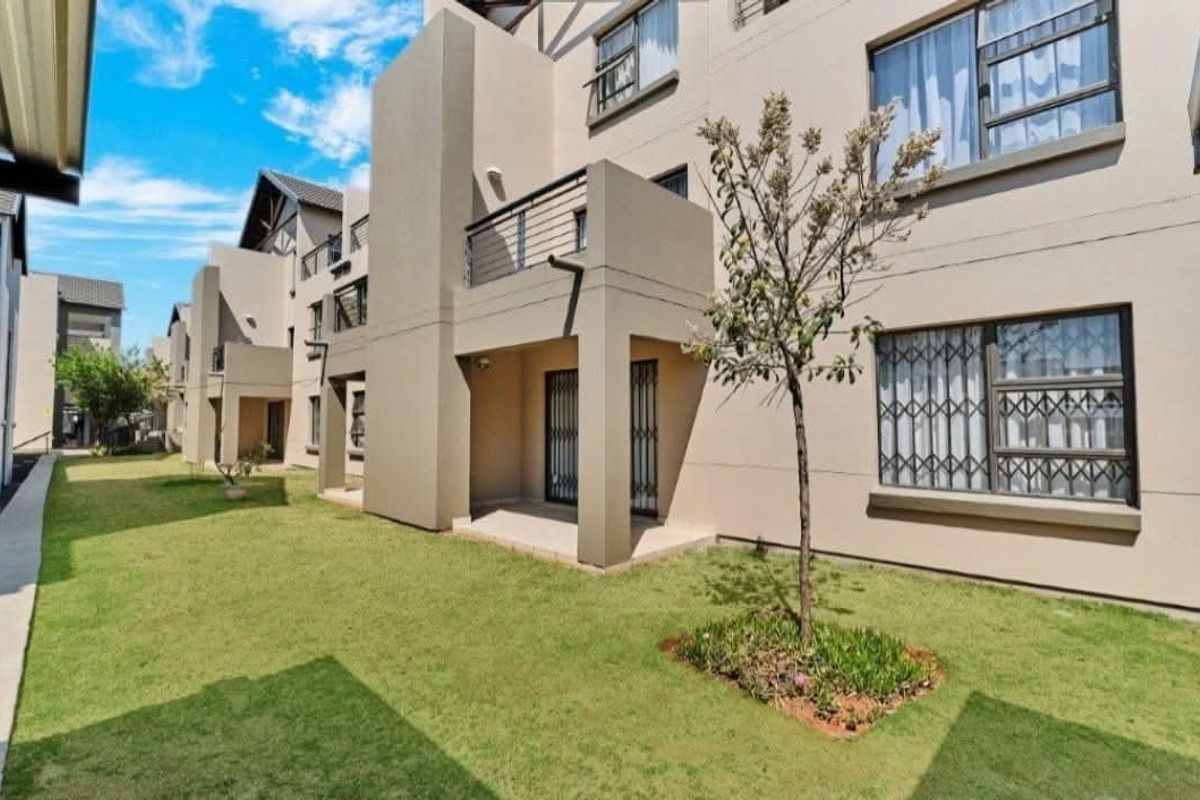 Rear view of a modern apartment complex featuring private balconies, security gates, and well-maintained communal garden areas.