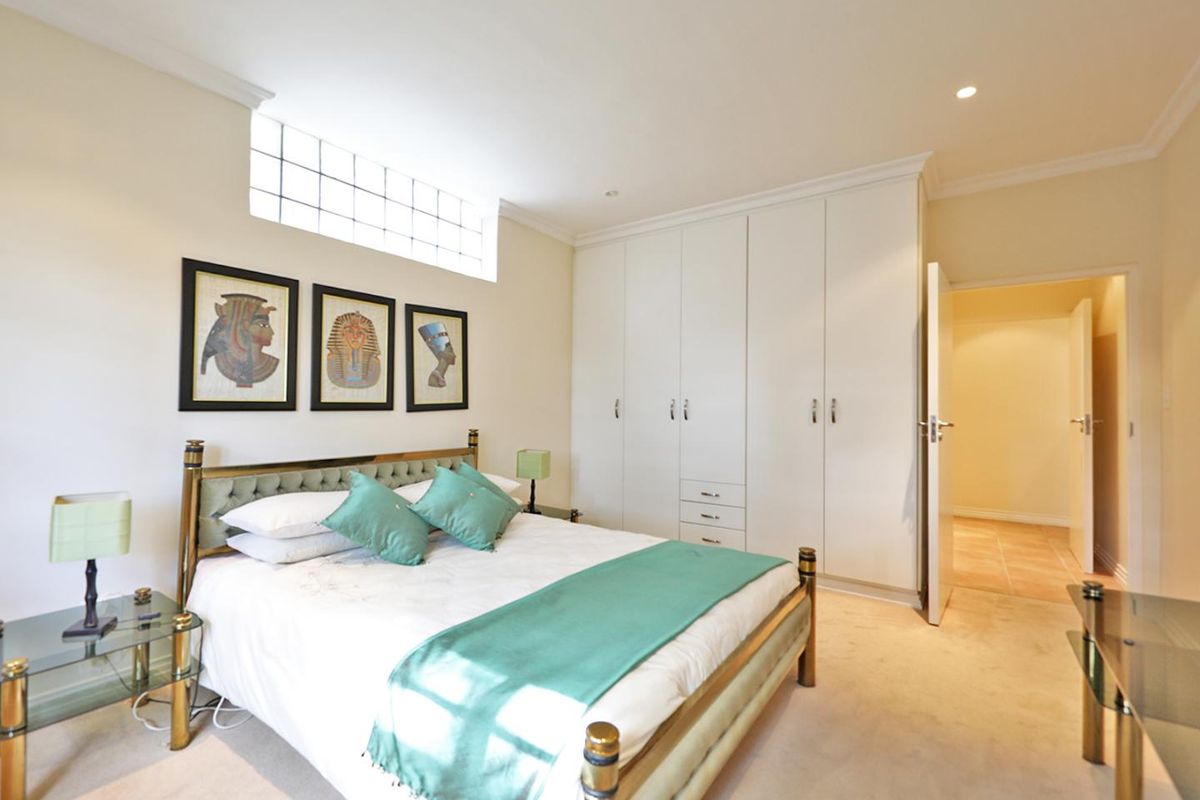 A well-maintained bedroom featuring built-in floor-to-ceiling wardrobes, recessed downlighting, and a high-level glass block window for natural light.