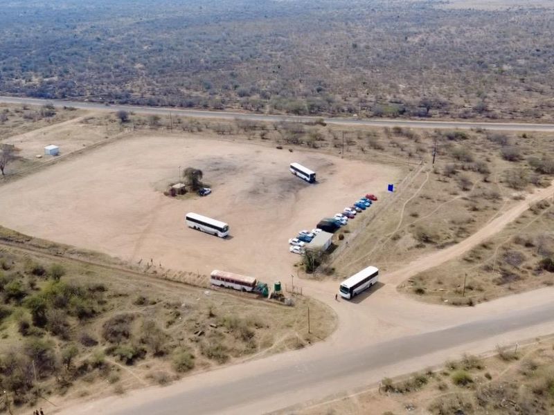 Aerial view of a large, open rural plot featuring unpaved ground, perimeter fencing, and direct access to a main road.