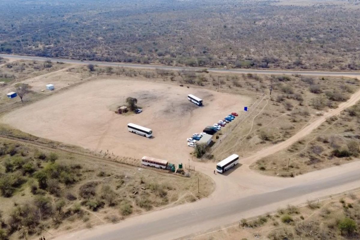 Aerial view of a large, open rural plot featuring unpaved ground, perimeter fencing, and direct access to a main road.