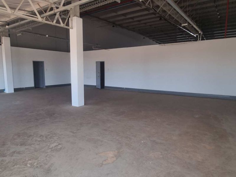Spacious industrial utility area featuring exposed steel roof trusses, concrete flooring, and structural support columns, suitable for various commercial or storage applications.