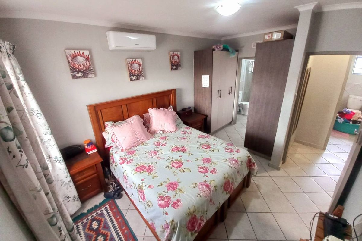 A bedroom featuring tiled flooring, a wall-mounted air conditioning unit, and built-in cupboards, with an adjoining en-suite bathroom visible.