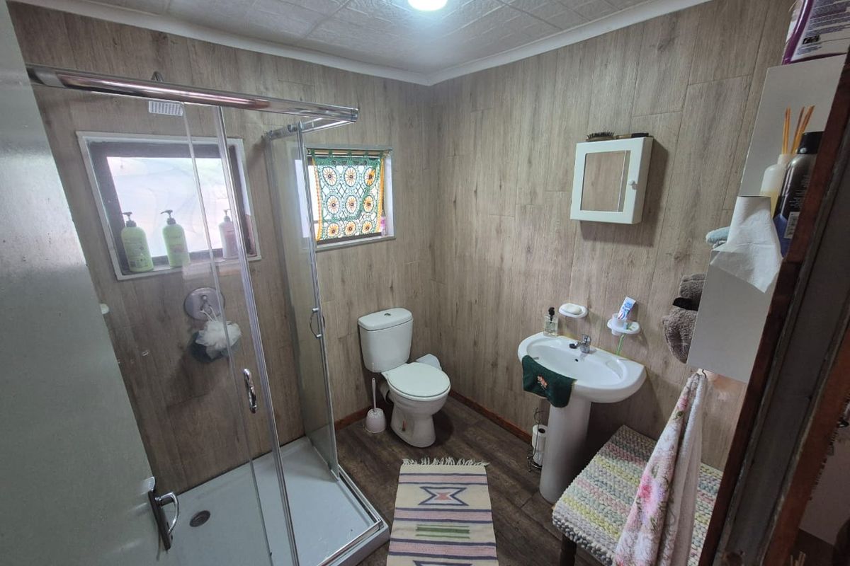 A functional bathroom featuring a glass-enclosed shower, pedestal sink, and toilet, finished with wood-look wall paneling and flooring.