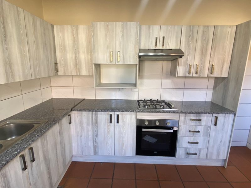 A functional kitchen featuring light wood-grain cabinetry, granite countertops, a gas hob, built-in oven, and tiled finishes throughout.