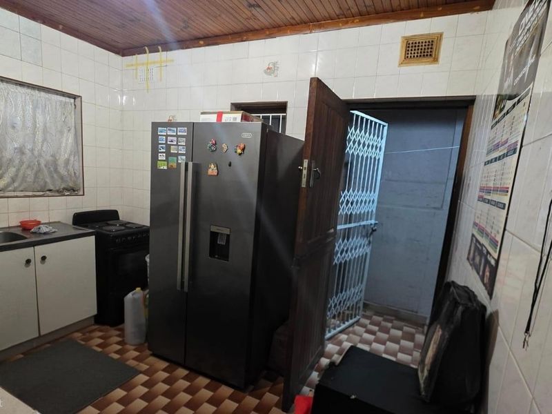 A functional kitchen space featuring tiled walls, a timber ceiling, and direct access to an exterior security gate.
