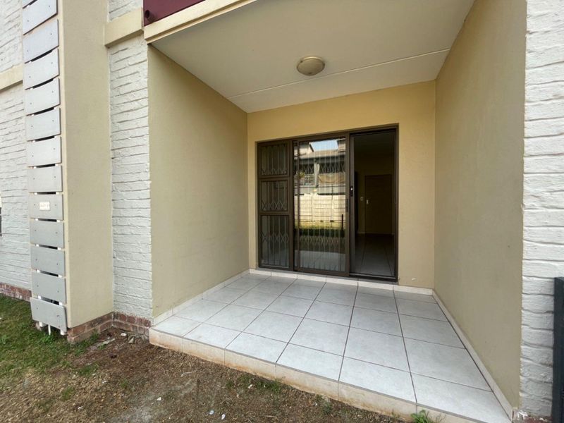 A covered patio area featuring tiled flooring, a sliding glass door with security gate, and direct access to the apartment interior.