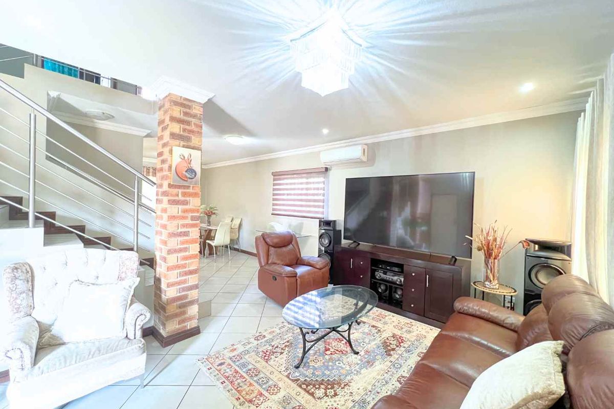 Spacious living area featuring tiled floors, an exposed brick pillar, and a staircase with a modern stainless steel balustrade.