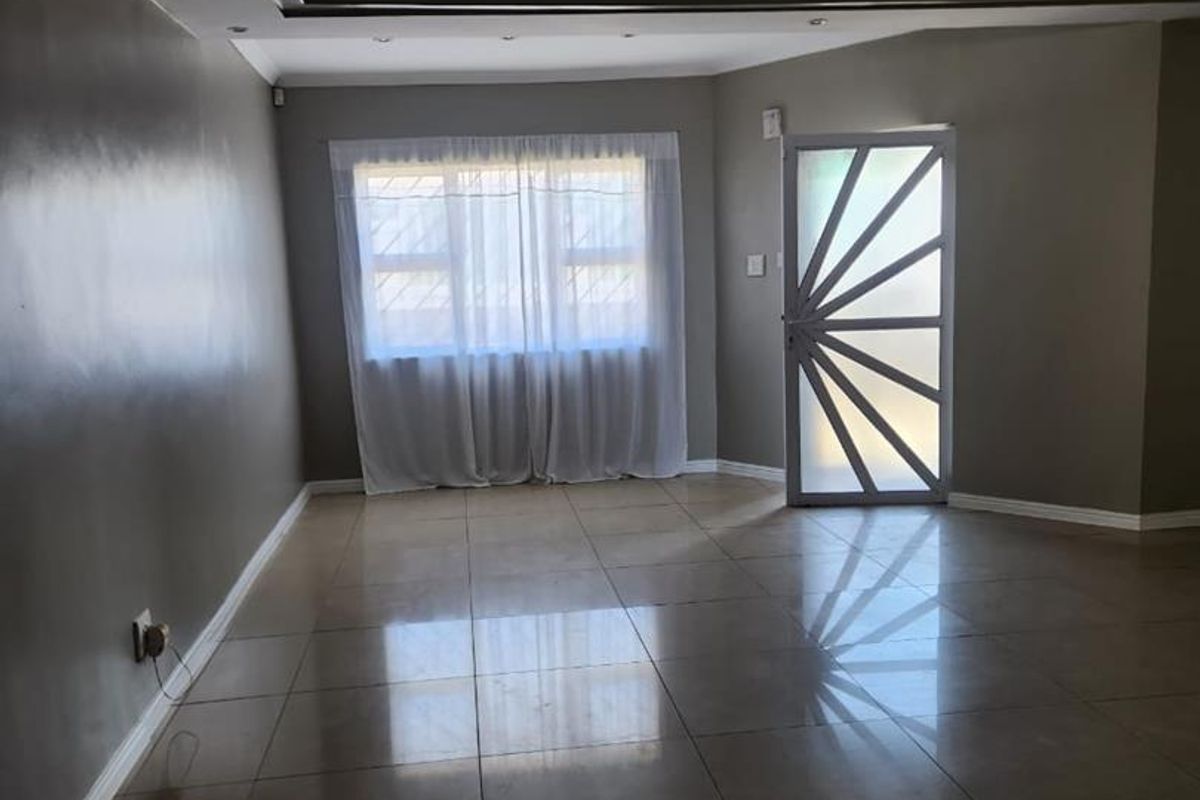 Spacious living area featuring polished tiled flooring, a modern drop ceiling with recessed lighting, and a decorative security entrance door.