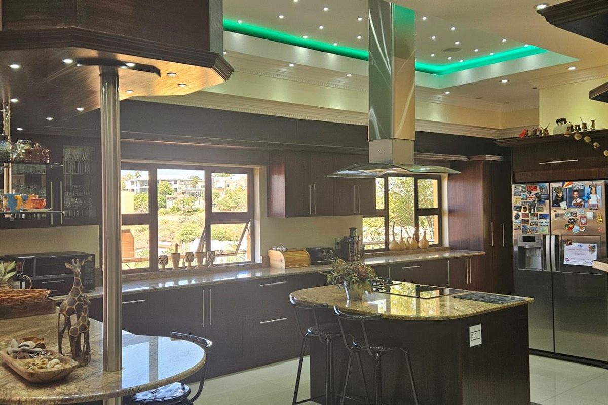Spacious kitchen featuring dark wood cabinetry, granite countertops, a central island with a cooktop, and integrated stainless steel appliances under a modern recessed ceiling.