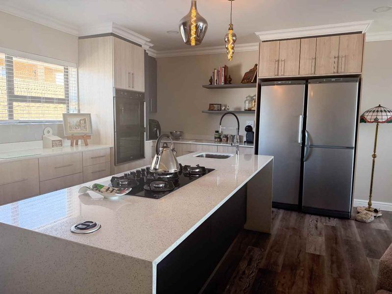Modern kitchen featuring a large island with a gas hob, quartz countertops, built-in oven, and stylish floating shelving with contemporary pendant lighting.