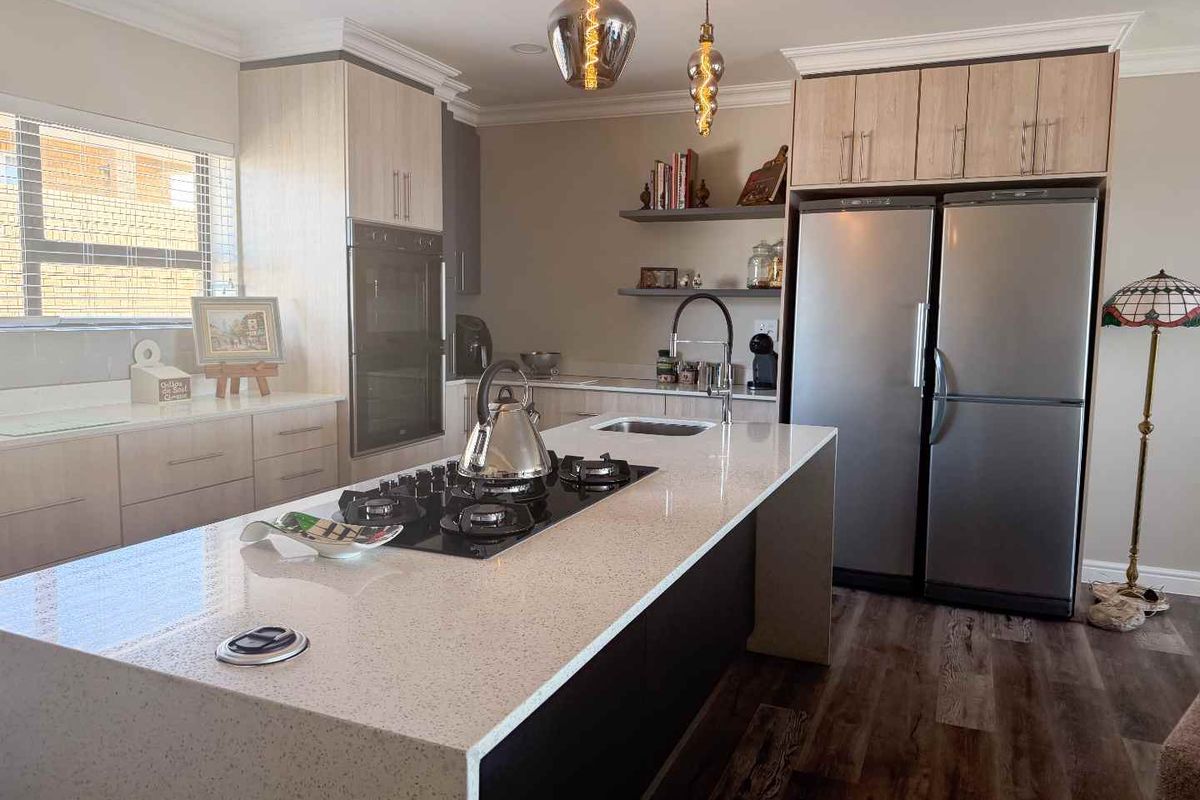 Modern kitchen featuring a large island with a gas hob, quartz countertops, built-in oven, and stylish floating shelving with contemporary pendant lighting.