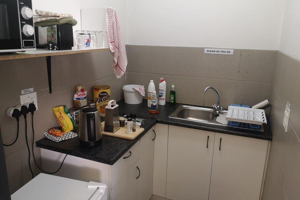 A compact kitchenette featuring built-in cabinetry, a stainless steel sink, and tiled backsplash, suitable for a small office or utility space.