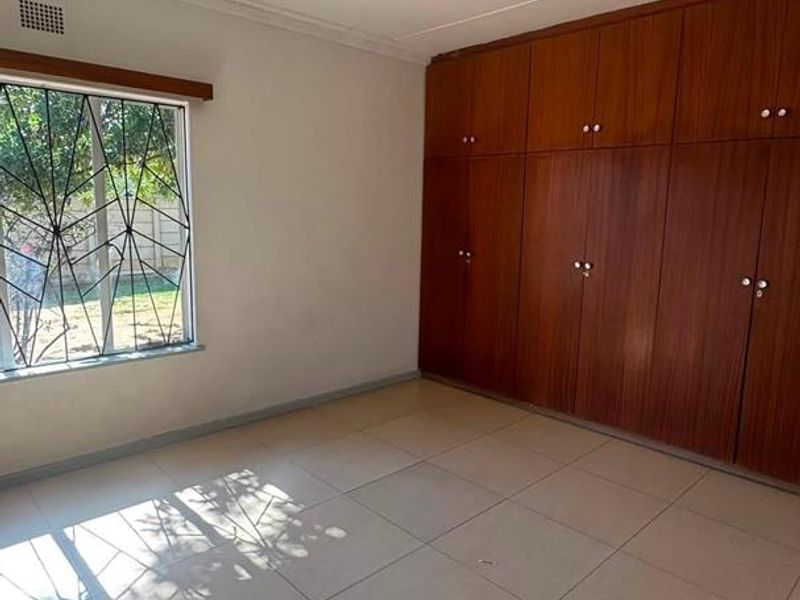 A vacant bedroom featuring tiled flooring, built-in wooden cupboards, and a window fitted with security bars.