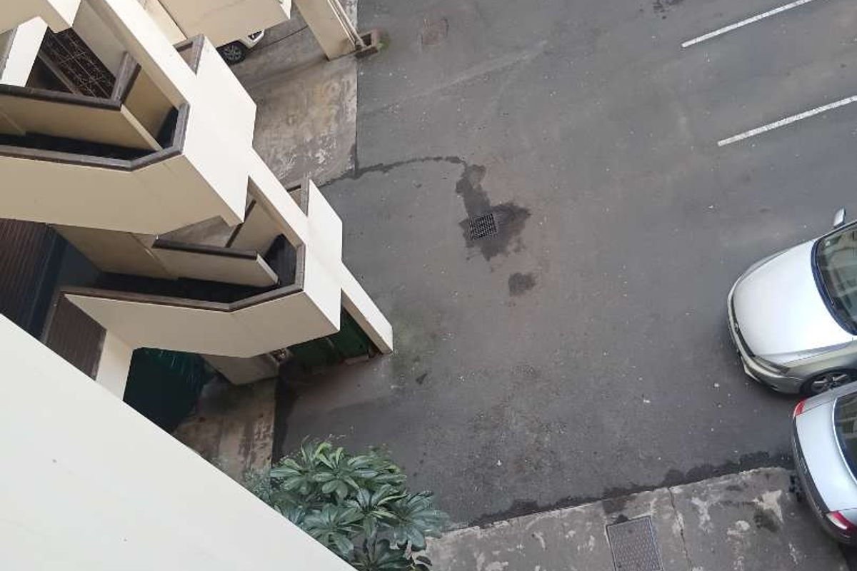 An elevated view of the apartment complex exterior, showing the parking area, concrete stairwell structure, and paved ground surfaces.