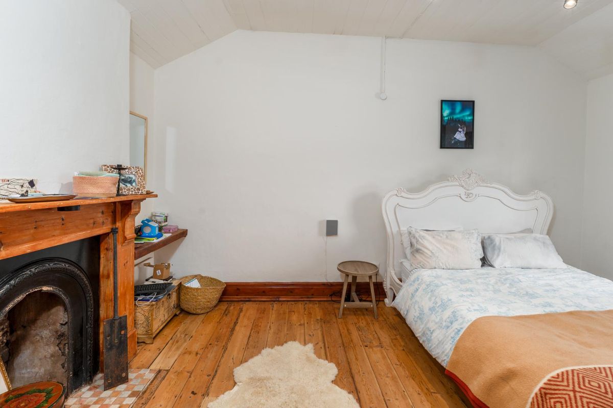 A bedroom featuring original timber flooring, a vaulted ceiling, and a classic cast iron fireplace with a wooden mantelpiece.