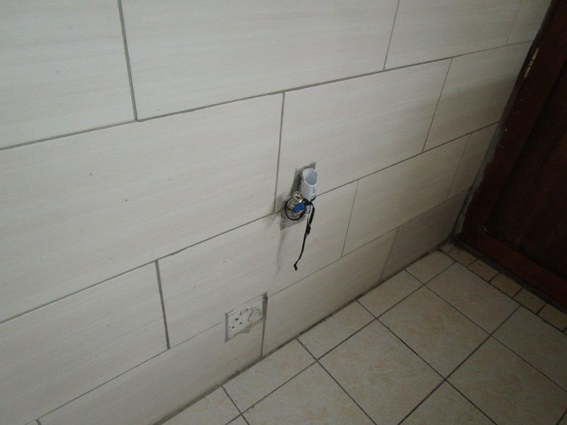 A utility area featuring tiled walls and flooring with exposed plumbing and electrical wiring requiring finishing and repair.