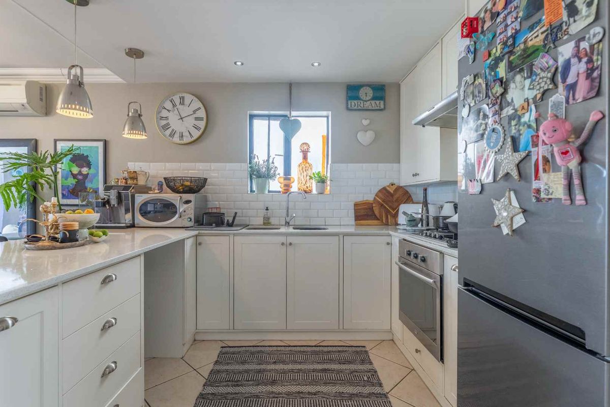 A well-maintained kitchen featuring white cabinetry, subway tile backsplash, stone countertops, and integrated stainless steel oven and hob.