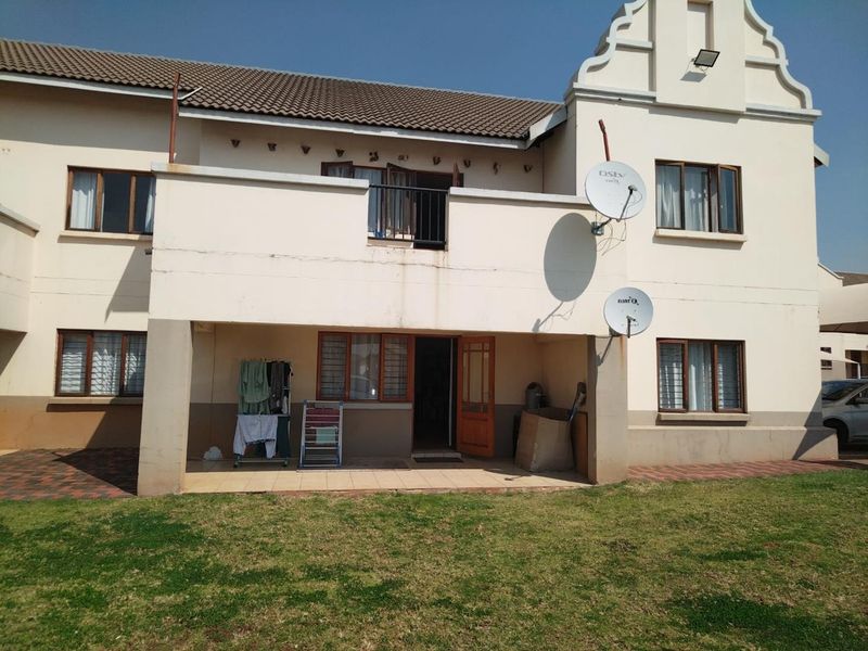 Rear view of the apartment building featuring a ground floor covered patio, an upper-level balcony, and a shared lawn area.