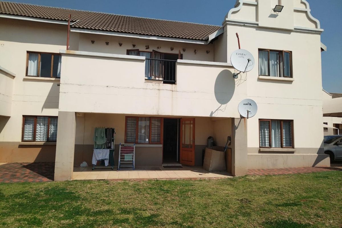 Rear view of the apartment building featuring a ground floor covered patio, an upper-level balcony, and a shared lawn area.