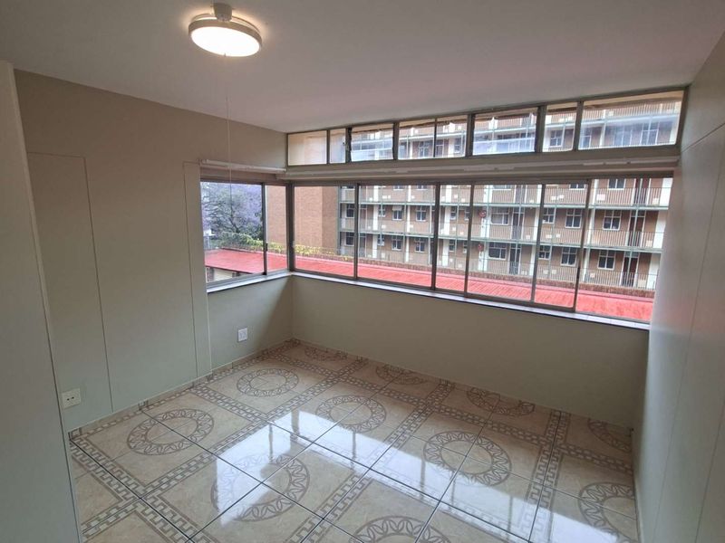 A bright, empty bedroom featuring large windows, tiled flooring, and built-in storage, offering a clean canvas for personalization.