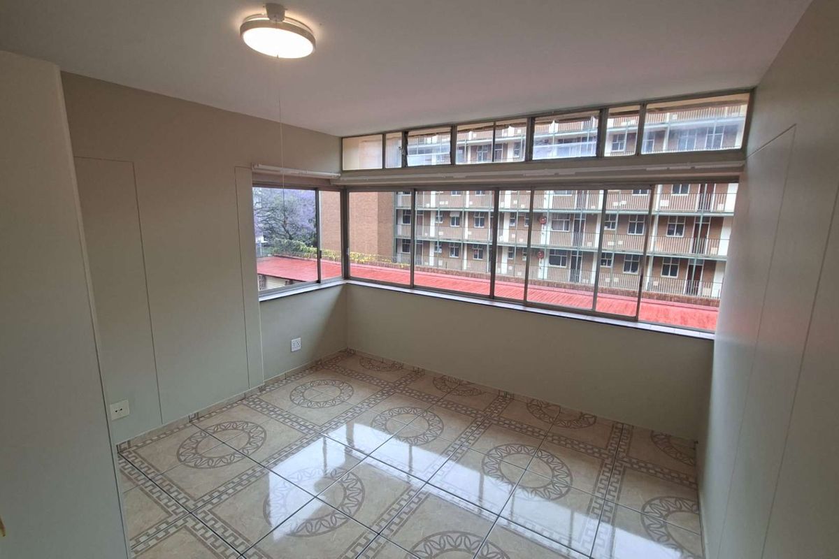 A bright, empty bedroom featuring large windows, tiled flooring, and built-in storage, offering a clean canvas for personalization.
